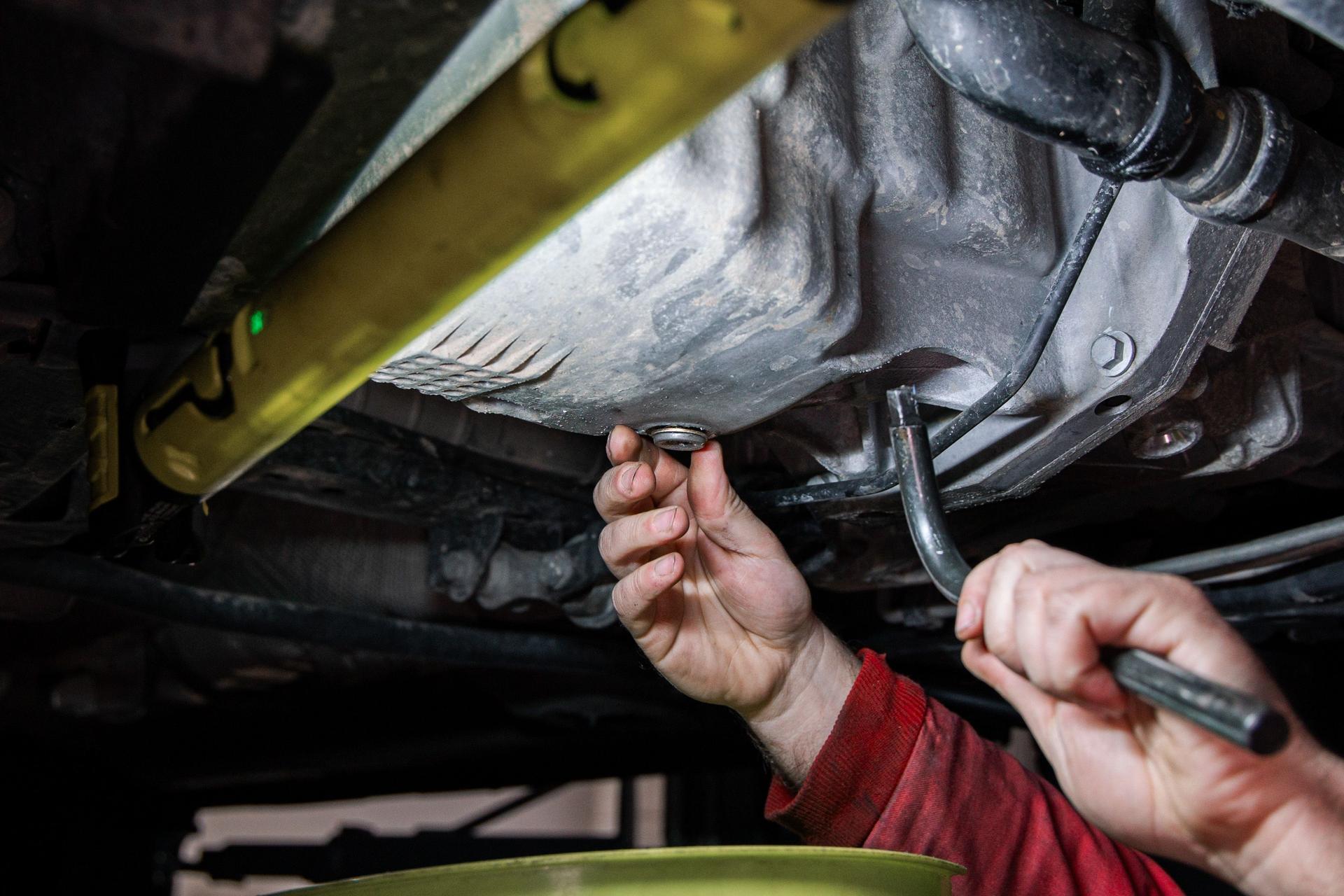 Mechanic Draining Engine Oil from Car During Oil Change in Auto Repair Shop