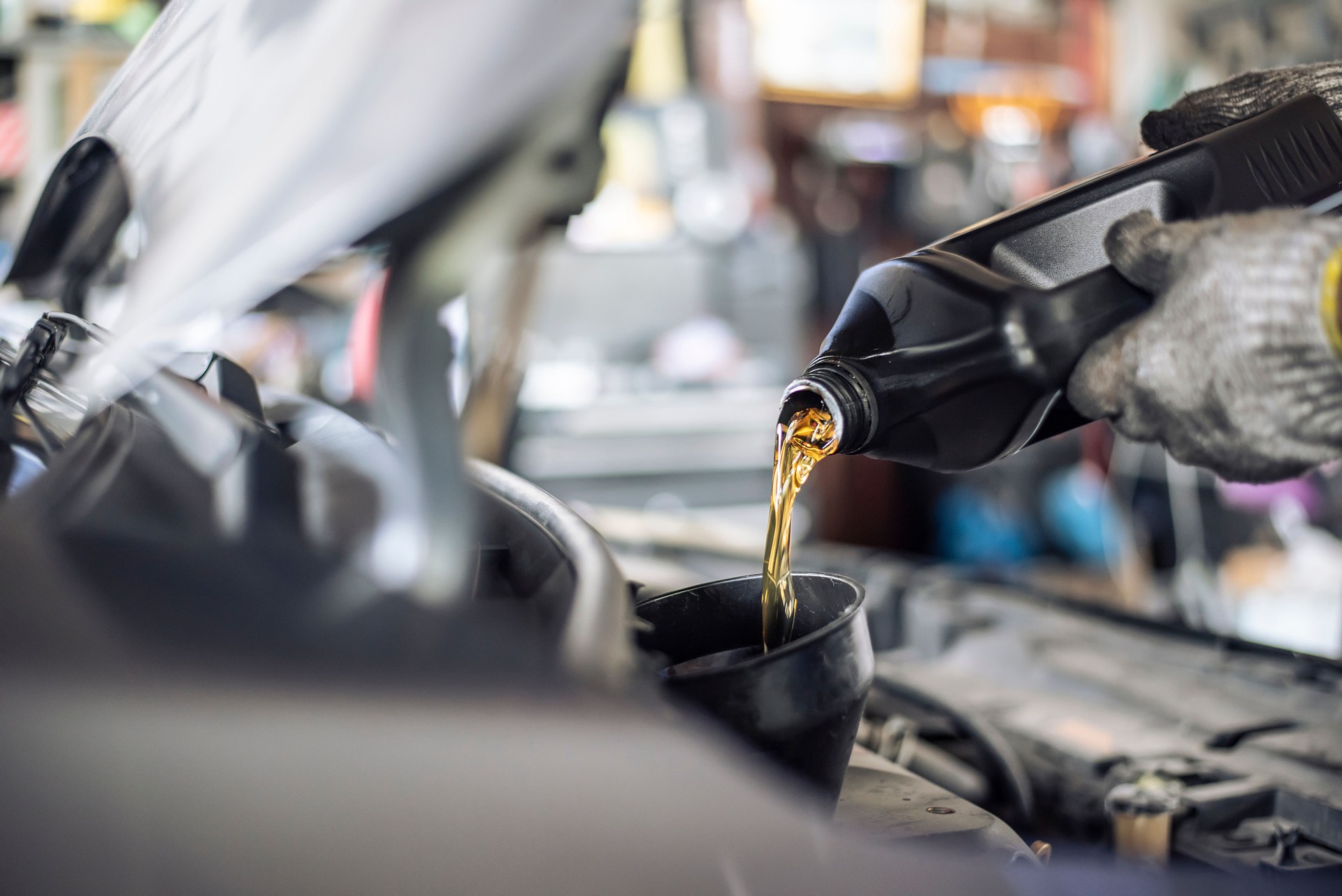 Close-up of a mechanic's gloved hands pouring new motor oil into a vehicle during a service check.