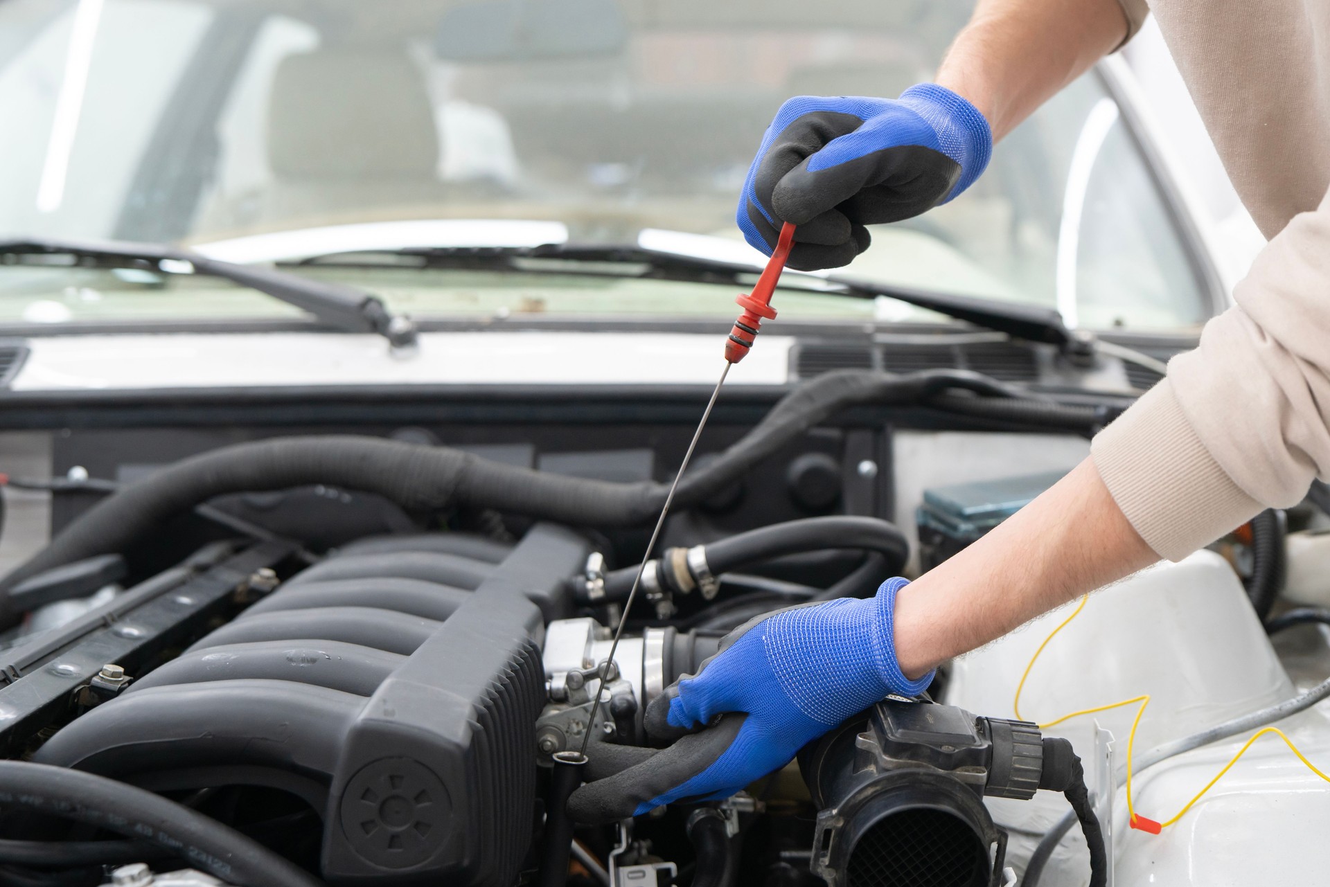 Mechanic uses a dipstick to check engine oil levels under the hood, ensuring vehicle operates efficiently and safely during maintenance checks.