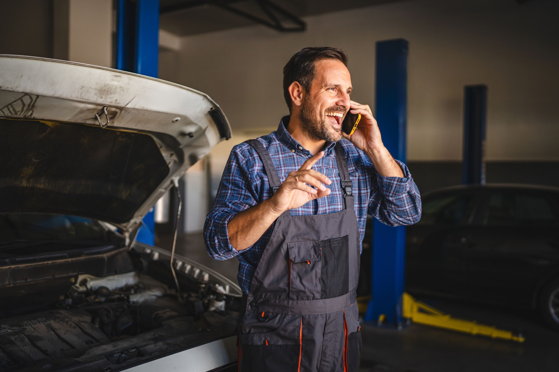 Adult smile man car mechanic talk on the mobile phone in the garage