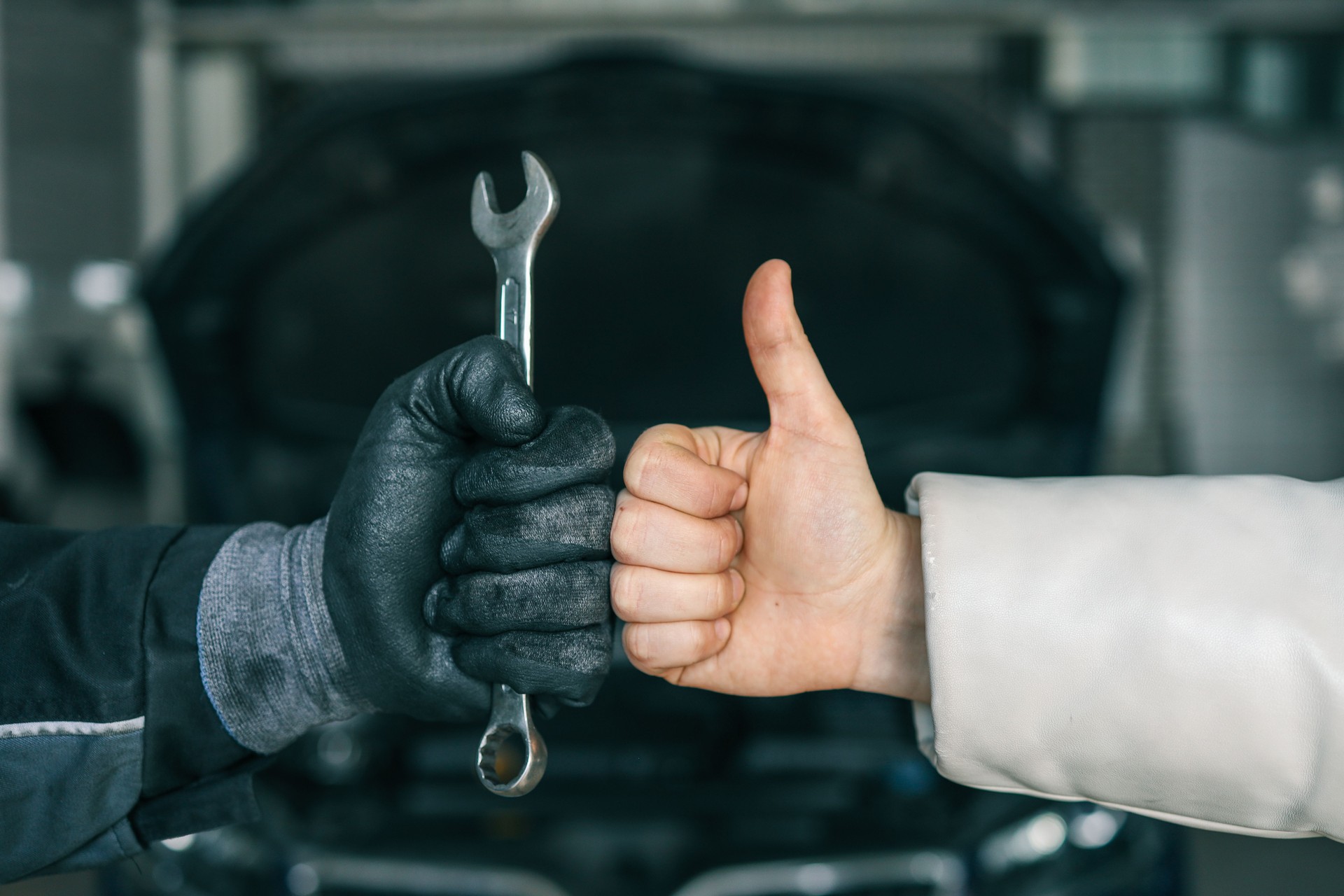 Close-up of a mechanic's gloved hand holding a wrench and a customer's hand giving a thumbs-up, symbolizing satisfaction and trust in car repair services